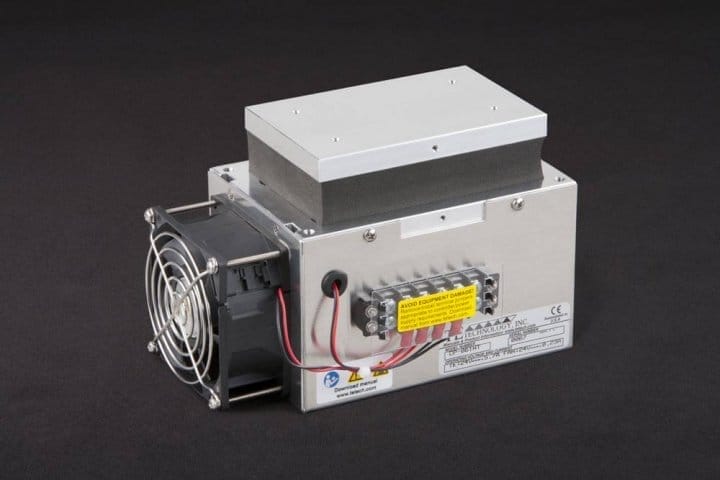 Three-quarter view of thermoelectric cold plate cooler/heater incorporating two thermoelectric modules. Cooled aluminum plate on the front, waste heat is exhausted to fins on back. Fins are fan cooled. The fan air enters on the one end of the fins, travels the length of the fins, and exhausts out the opposite side. Operates on 24 volts DC and removes 59 watts of heat at a 0°C temperature difference relative to ambient. Internal extender blocks improves the heat pumping capacity at larger temperature differences. Can heat to 100°C without damaging the cooler.